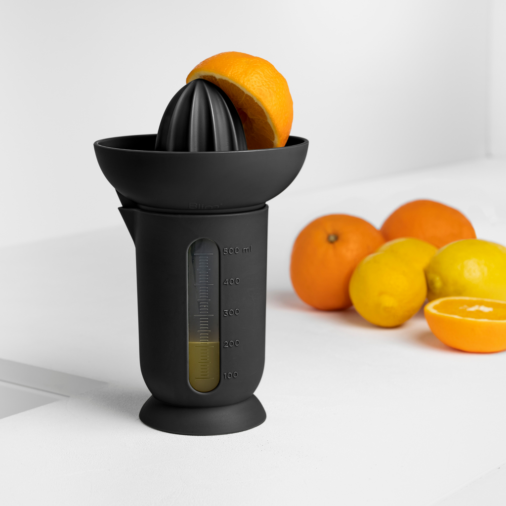 Blim+ UFO Juicer with QB Carafe in black, beside fresh oranges